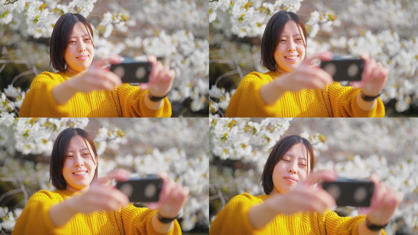 年轻女子用智能手机与大自然中的樱花树自拍
