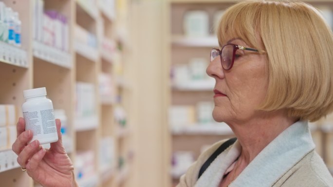 老妇人正在检查从药店货架上拿的药瓶