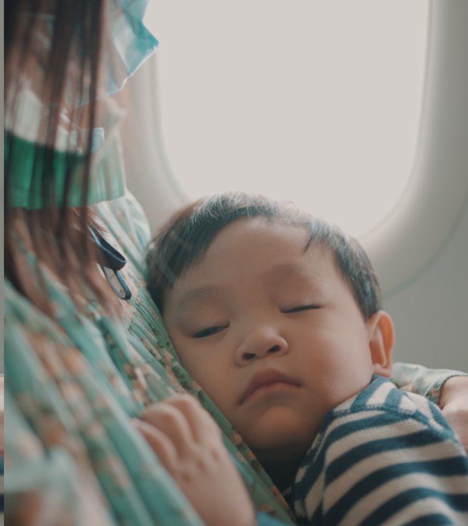 坐飞机旅行时，男孩睡在妈妈的怀里。