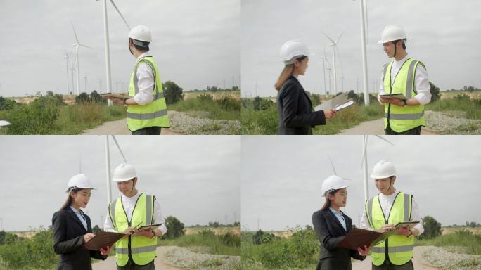 风力发电站技术工程师。穿着反光夹克和头盔的亚洲男工程师和女商人走进风力发电厂。手动签名文件夹中的文档