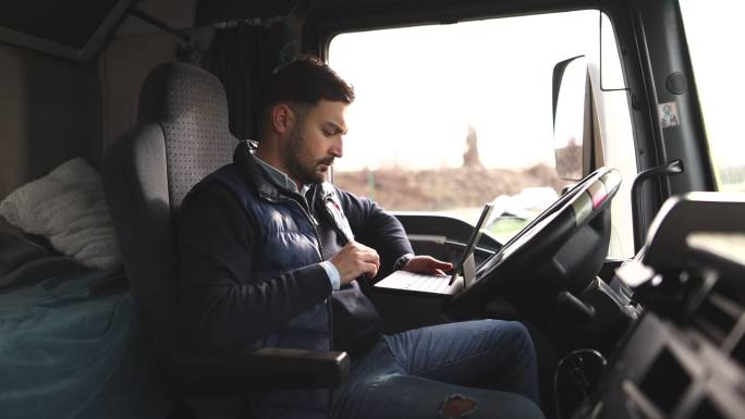 卡车司机坐在驾驶室中在平板电脑上键入目的地