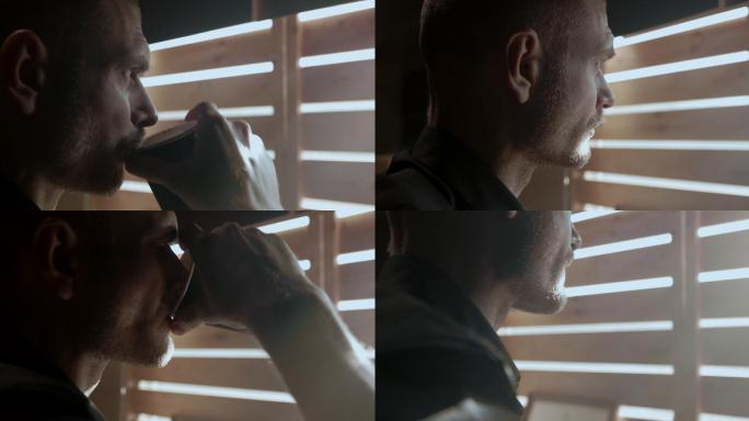 清晨，一个穿黑衬衫的男人站在窗前喝咖啡