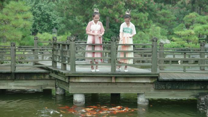 女孩们穿着汉服，在公园里喂锦鲤。