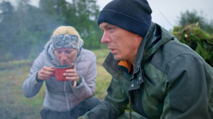 男女野外生存专家坐在营火旁喝茶