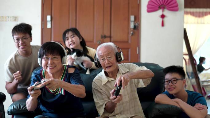 2名亚裔中国祖父母与孙子孙女在家玩电子游戏。
