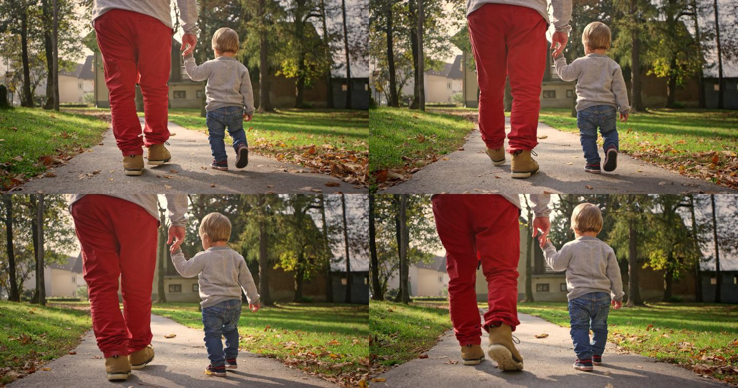 斯洛莫蹒跚学步的孩子在阳光下牵着父亲的手指在公园里散步