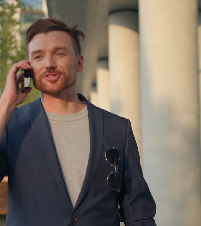 一位穿着蓝色西装、带着皮质笔记本电脑包、魅力四射的年轻商务人士微笑着在智能手机上交谈