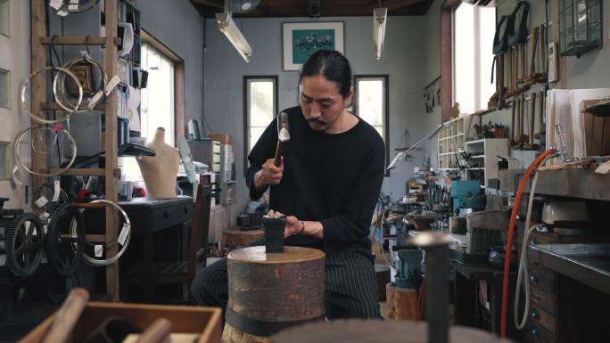 一位中年银匠在准备制作珠宝时锤击银器的缓慢推拉镜头