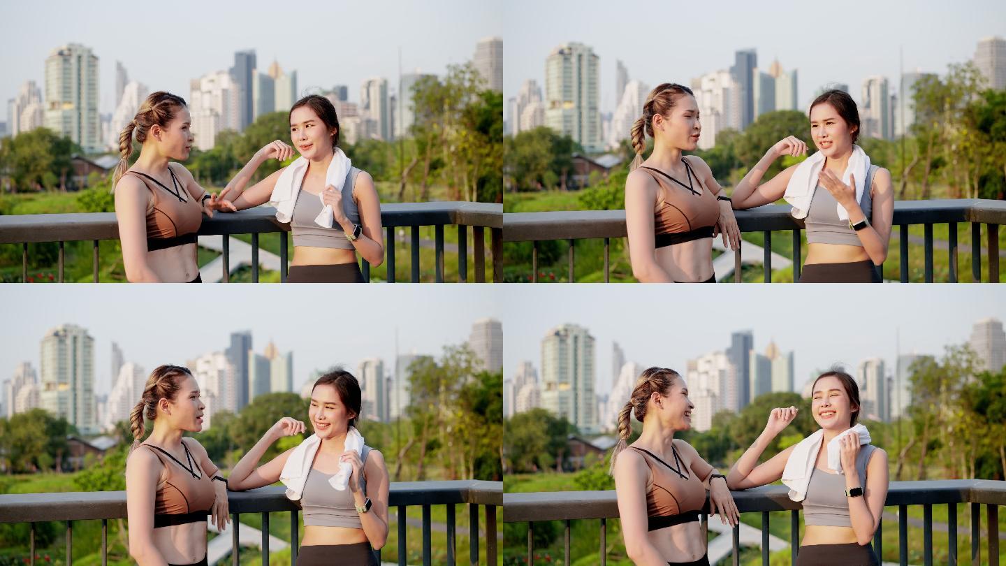 两位穿着运动装的亚洲美丽中年女性朋友在一起健身后，在市中心附近的公园花园的人行天桥上聊天，积极的生活