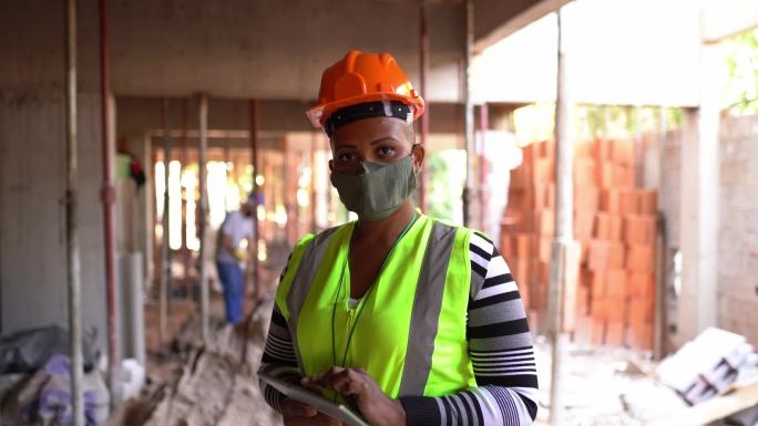 一名女性建筑工人在施工现场使用数码平板电脑并佩戴防护面罩的肖像
