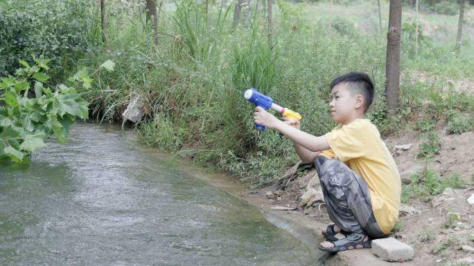 4K一个小男孩在小溪边玩水枪