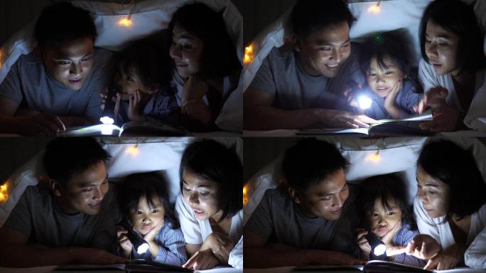 小女孩睡觉前和父母在毯子下看书