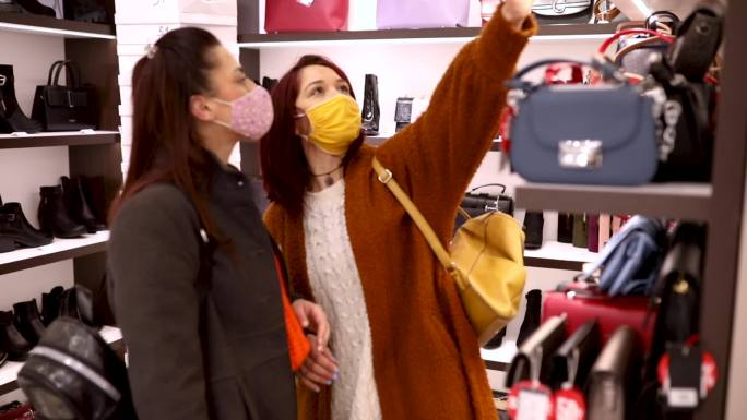 迷人的年轻女子在购物时玩得很开心，两人都戴着防护面罩，这是一种新的常态