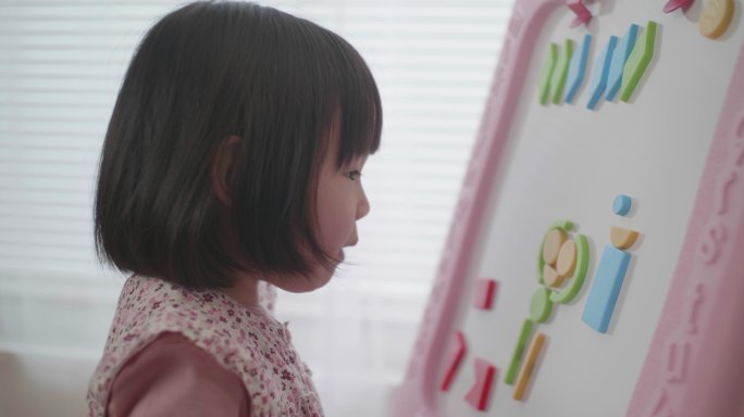 蹒跚学步的女婴在白色背景的白板上玩形状玩具块