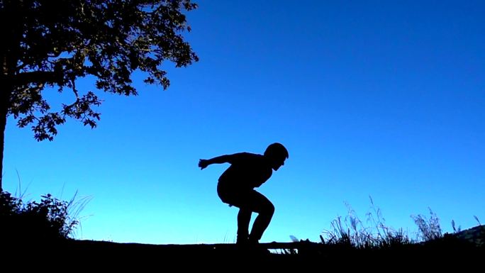 SLO MO Man剪影在蓝天下跳跃和踢腿