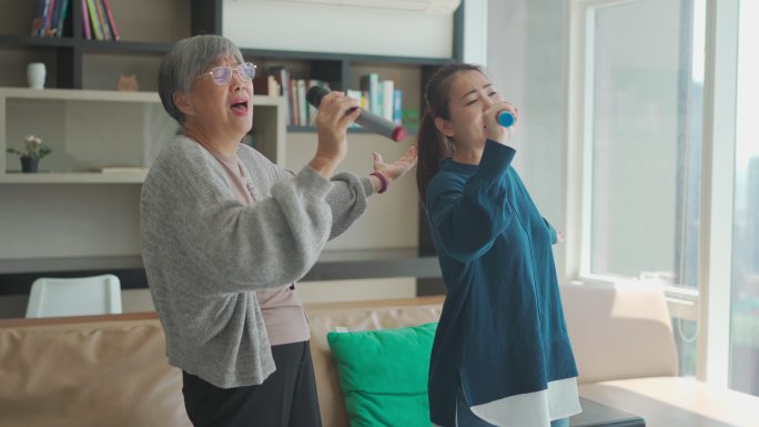 周末休闲活动期间，亚裔华人老太太与女儿在客厅唱卡拉OK跳舞