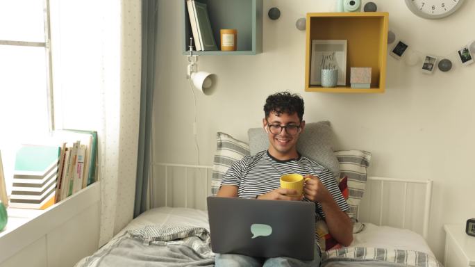 大学生节坐在床上看电脑喝水水杯打招呼聊天