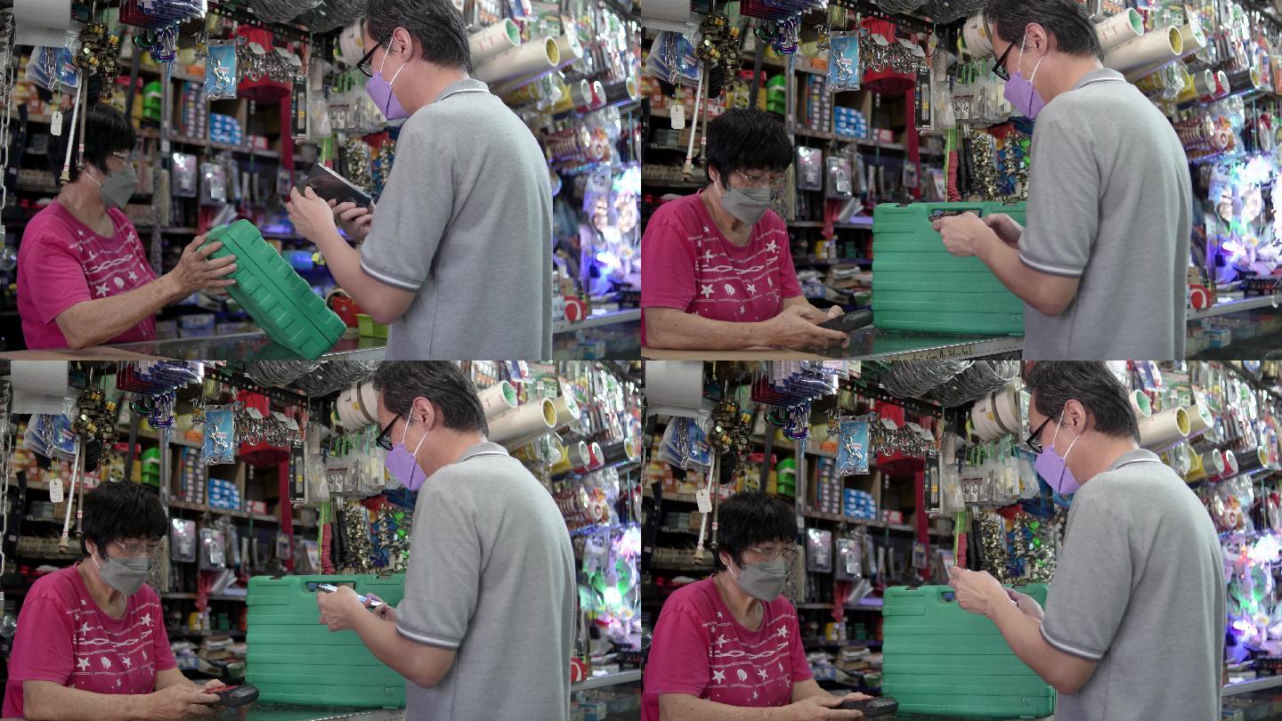 一名亚裔中国男子在商店用手机付款-购买硬件电动工具