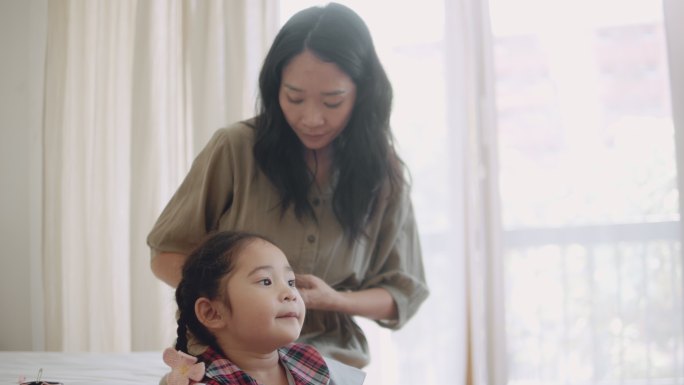 一位亚洲母亲为准备上学的女儿做辫子。