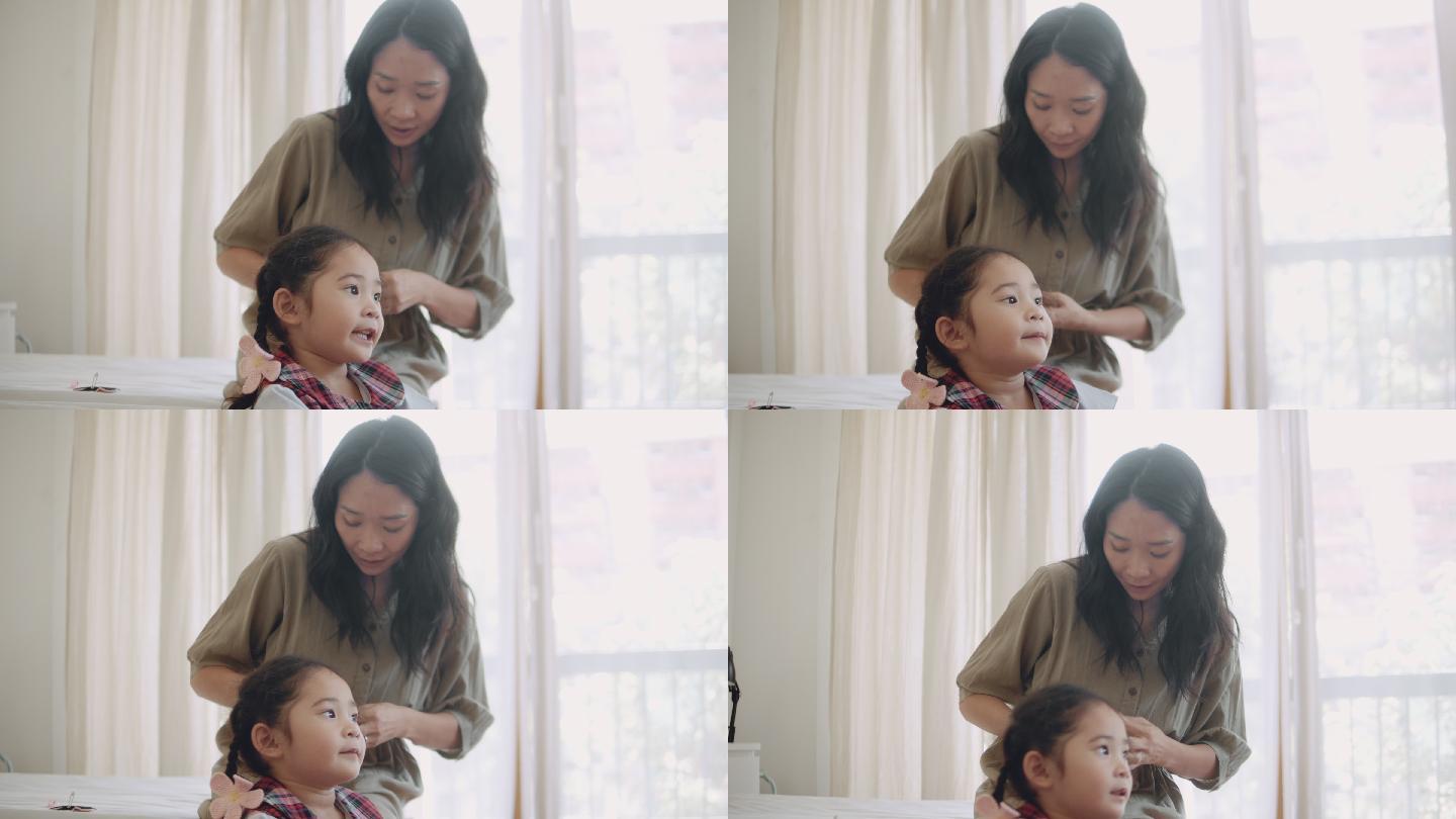 一位亚洲母亲为准备上学的女儿做辫子。