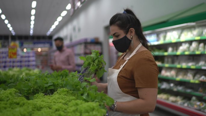 一名戴着口罩的年轻女子在超市整理产品