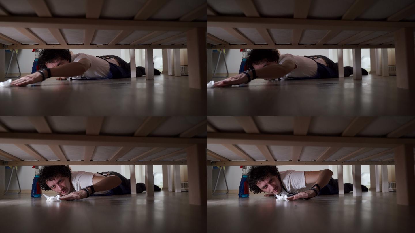 一个年轻人躺在地板上，在床下擦地板