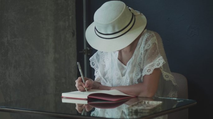 戴着白帽子的美丽艺术家在笔记本上画素描，她的作品在家里反射着玻璃桌