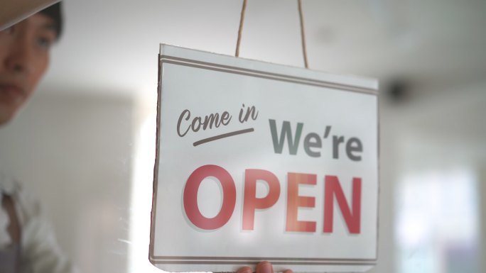 亚洲商店员工开业玻璃门上的开放标志