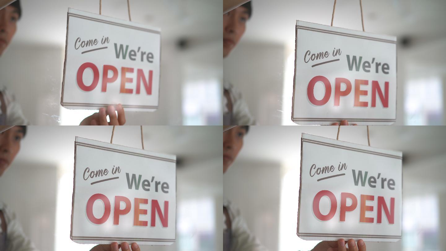 亚洲商店员工开业玻璃门上的开放标志