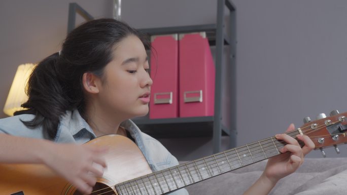 微笑的少女在家的客厅里弹原声吉他。创造性爱好