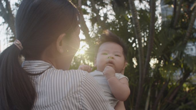 亚洲母亲在夕阳下亲吻她的新生男婴，同时在室外公园放松。