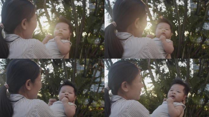 亚洲母亲在夕阳下亲吻她的新生男婴，同时在室外公园放松。
