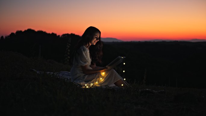 黄昏在草地上看书的慢镜头年轻女子