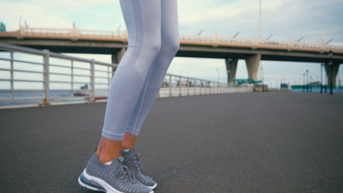 一位穿着白色紧身裤的年轻女运动员的双腿在柏油路上跳跃