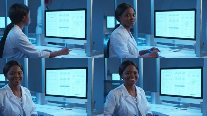 一位年轻的黑皮肤实验室医生面带微笑，坐在她的工作场所，在一个现代化的实验室里用电脑显示器拍照