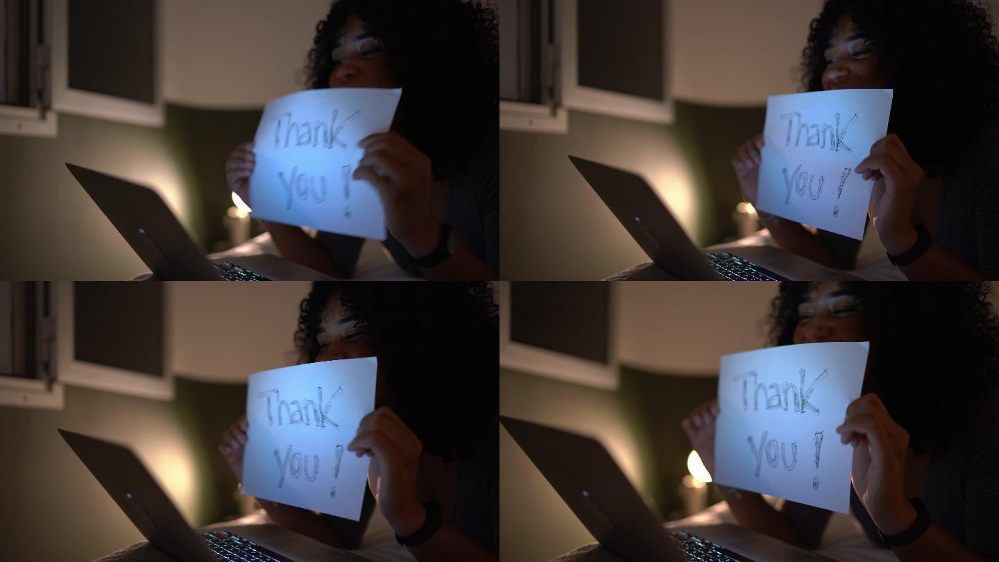 年轻女子在家打视频电话，展示写着“谢谢”的纸