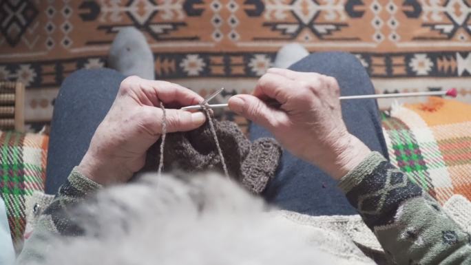 POV。一位老年人编织精细美观，一位奶奶双手布满皱纹的特写镜头，正在制作一件新的冬季毛衣，积极的退休