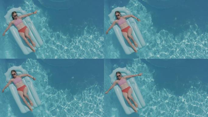 一个戴着墨镜的女人躺在游泳池里的蓝色充气床垫上。