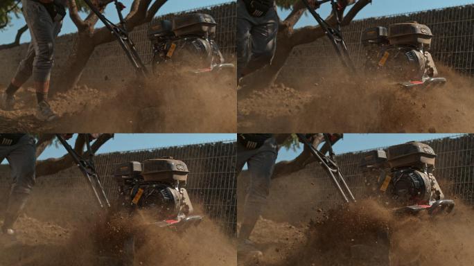 SUPER SLO-MO园丁使用前齿耕耘机沿着铁丝石笼岩石围栏犁过土壤