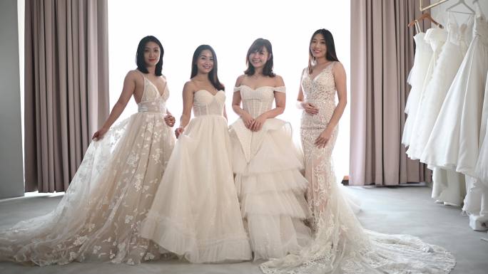 美丽的亚裔中国新娘和伴娘在婚纱店看着摄像机，开心地微笑着