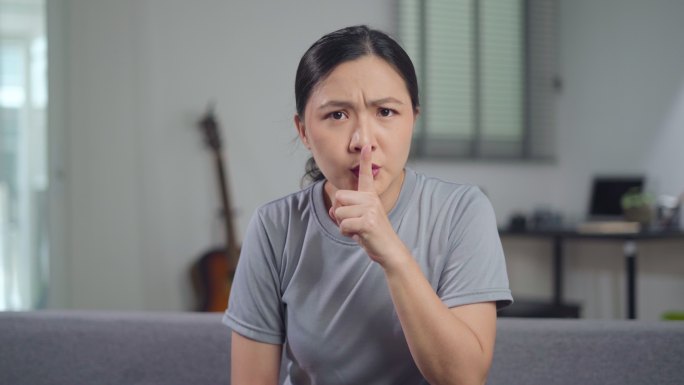 亚洲女性把食指放在嘴唇上意味着坐在家里的沙发上保守秘密。