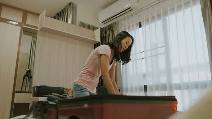 快乐的亚洲女人在家把手提箱放在床上。