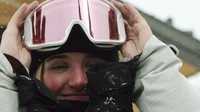一位微笑的十几岁女子滑雪运动员戴上护目镜，准备在阴天滑雪