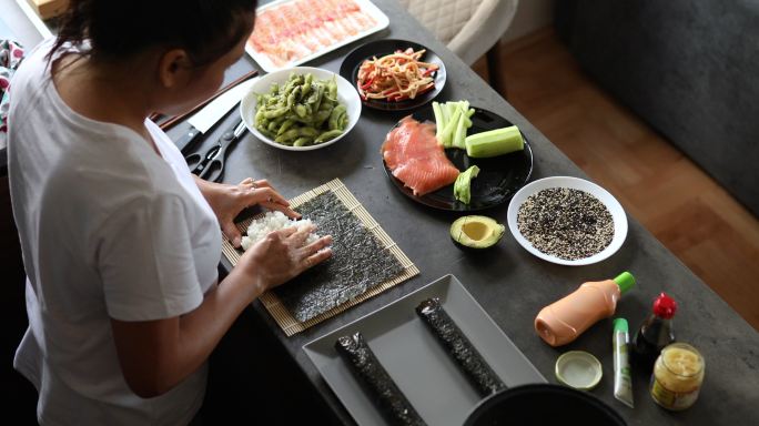 熟练的泰国女人，把寿司米饭放在海苔上，准备午餐用的寿司卷