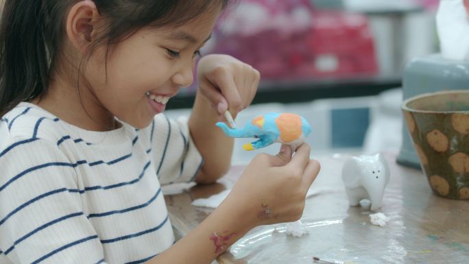 亚洲小女孩的慢镜头有趣地在陶瓷小象上画油画。学校开设儿童工艺美术创意活动课。