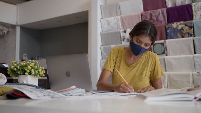 因新冠肺炎流行，一名年轻女子戴着防护口罩在工作室制作新时装系列
