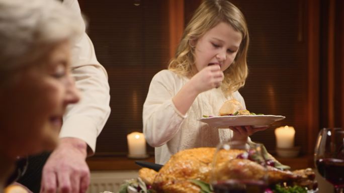 孩子在享受她的感恩节火鸡片，她的爷爷为她服务