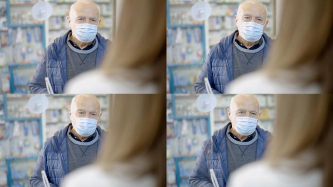 戴口罩的老人站在药房里，一边说话一边接受女药剂师的建议