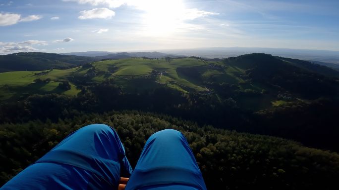 双腿可见的滑翔伞飞行期间的山脉鸟瞰图