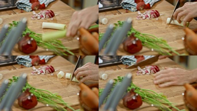 男厨师的双手在厨房的木板上切韭菜